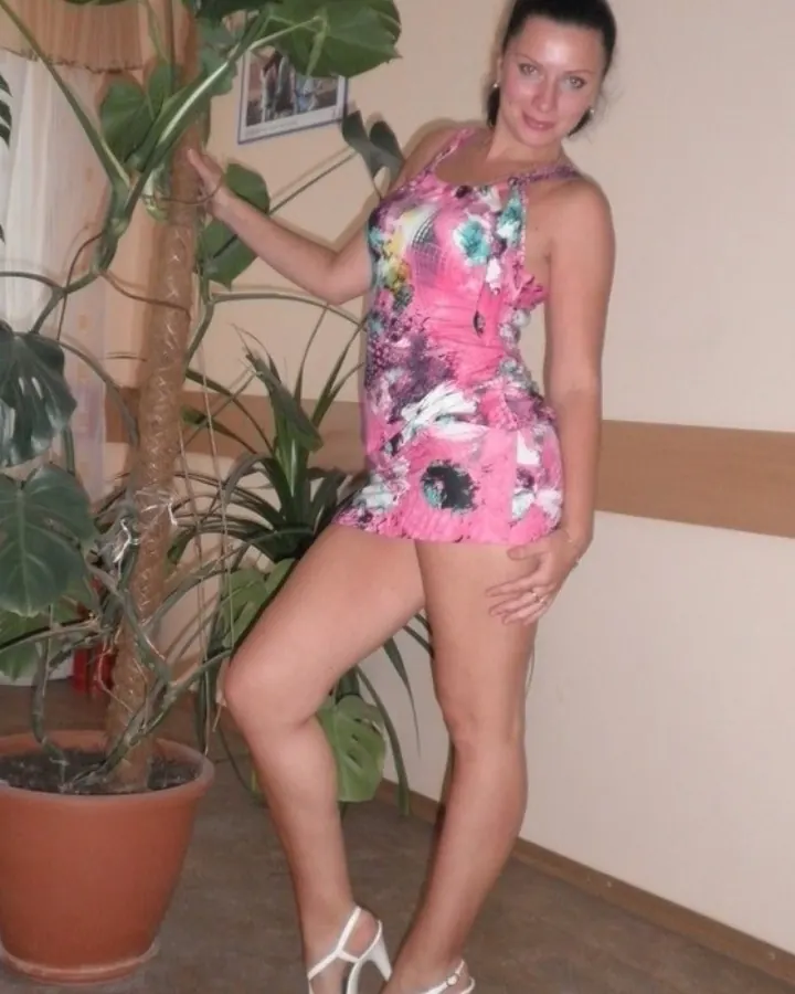 Femme aux cheveux bruns, portant un corset noir et des collants en latex noir, posant dans une pièce violette