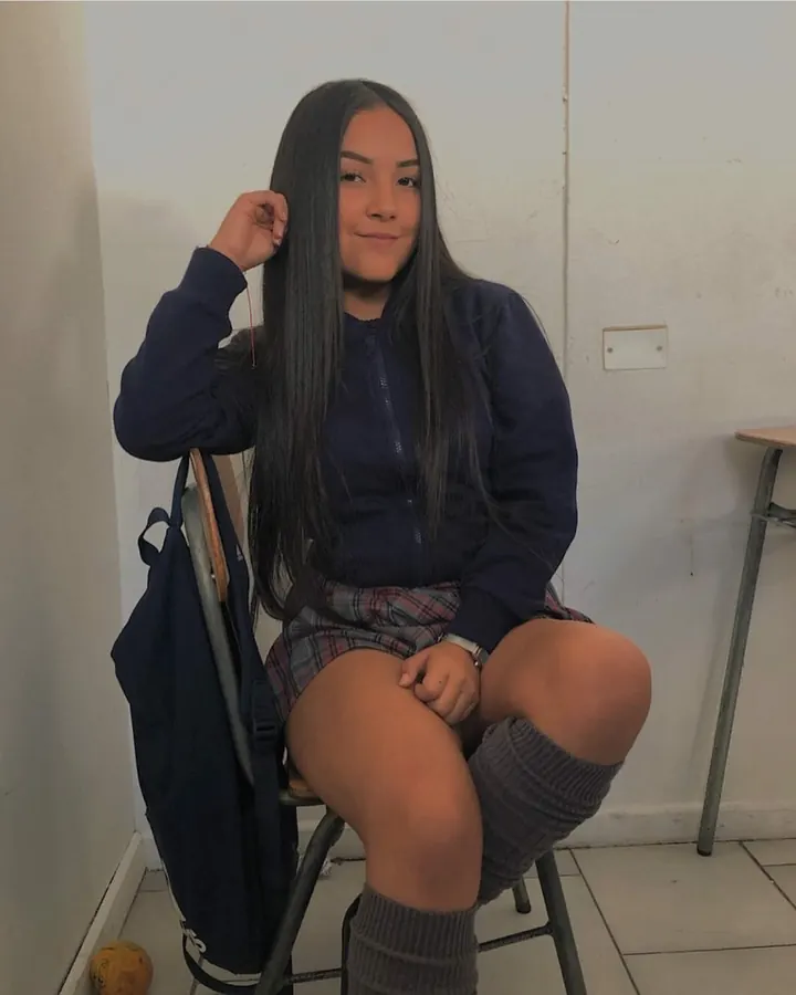 Jeune femme aux longs cheveux noirs, assise sur une chaise, portant un sweat bleu foncé et une jupe à carreaux