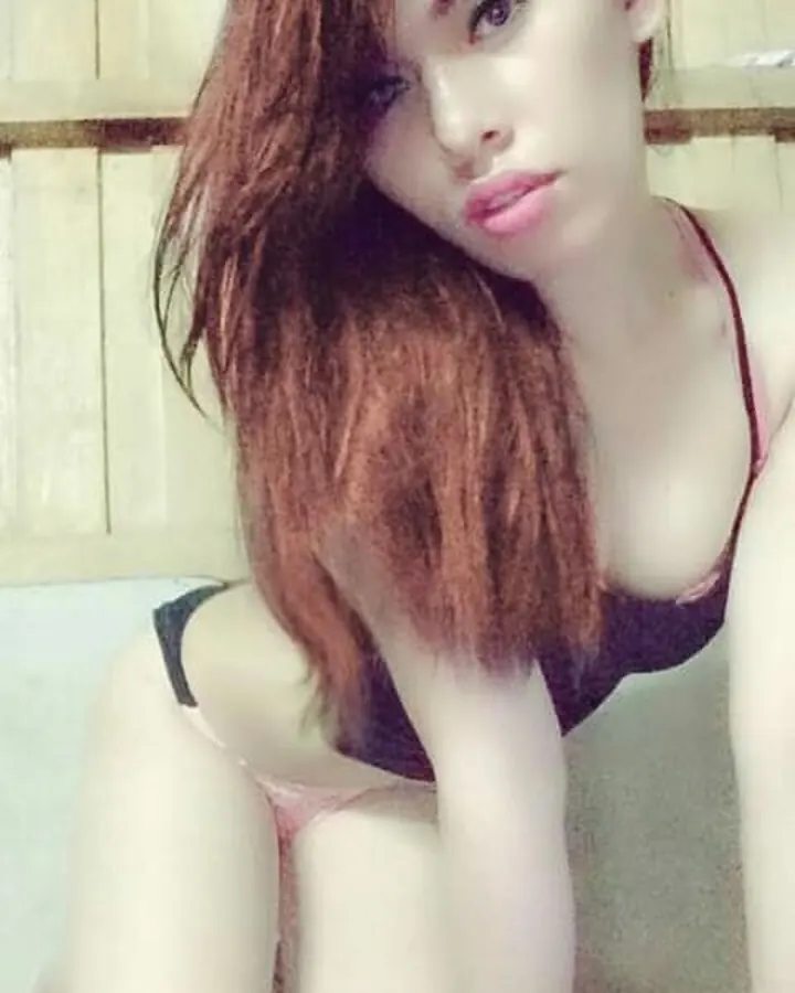 Femme en haut noir, jupe grise, posant dans une salle de bain, tenant un appareil photo.