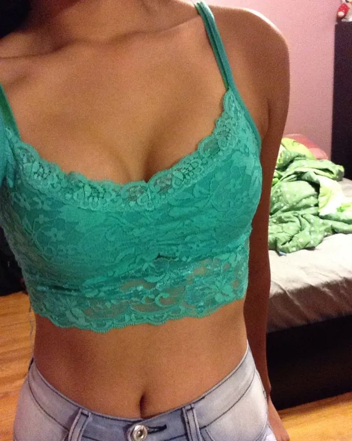 Vue rapprochée d'une femme portant un haut en dentelle turquoise et un jean clair, dans une chambre.