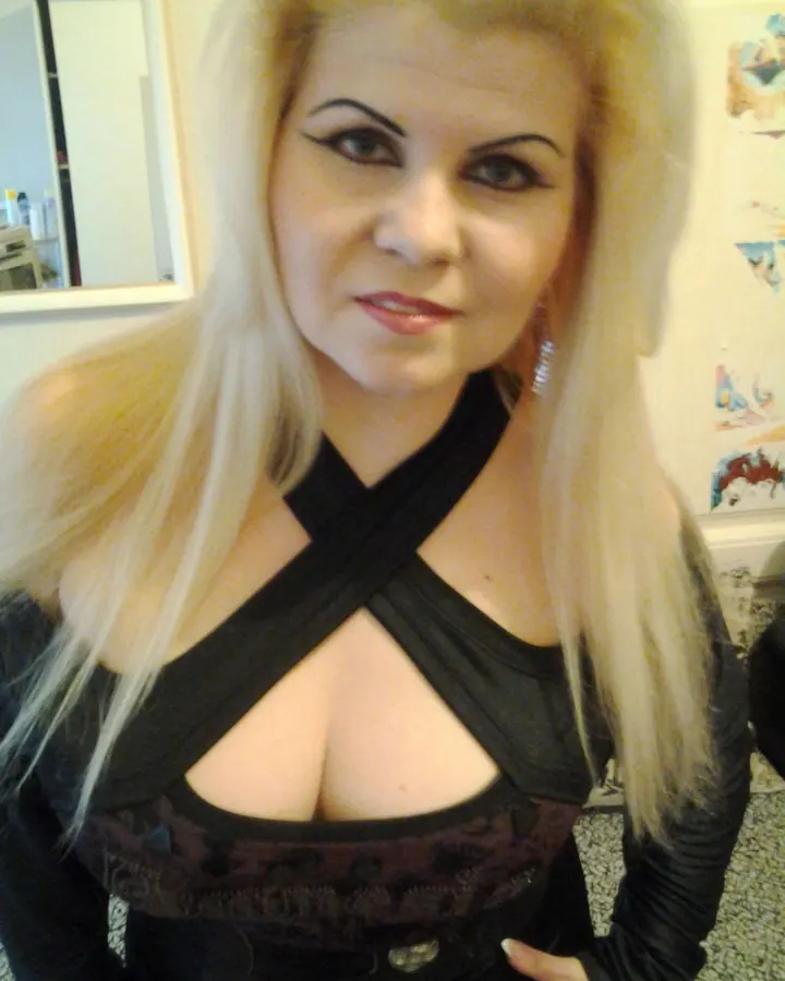 Femme aux cheveux blonds platine portant un haut noir à découpes, regardant l'objectif avec un sourire discret.