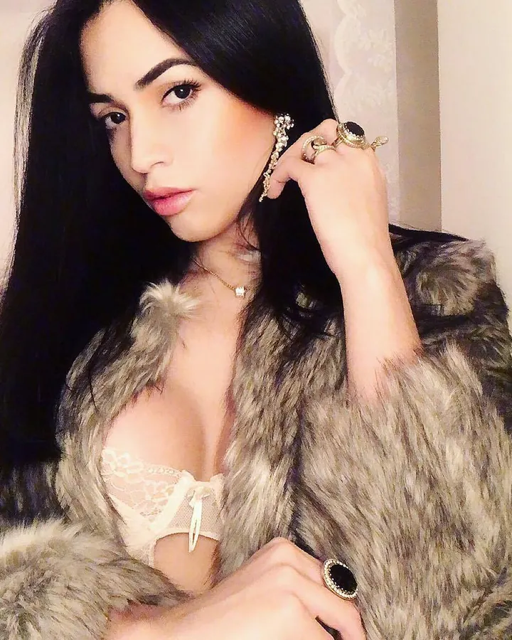 Femme en fourrure grise, soutien-gorge blanc, regardant la caméra, main sur la joue.