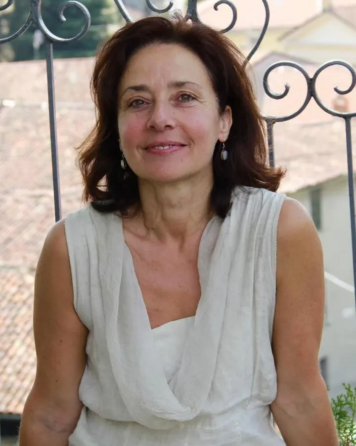 Femme aux cheveux bruns, portant une robe blanche sans bretelles et des gants noirs, assise sur une chaise.