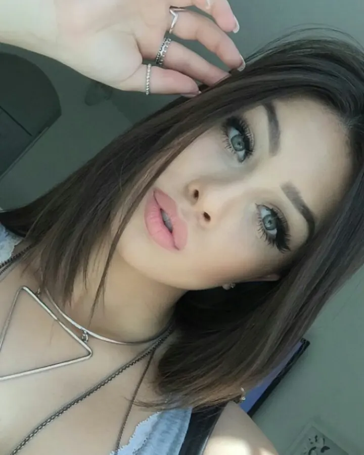 Jeune femme aux cheveux noirs, portant un haut blanc et un collier, regardant l'appareil photo.