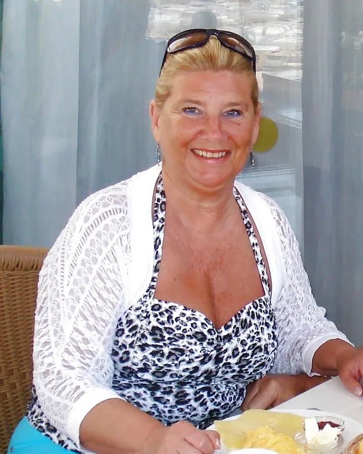 Femme aux cheveux blonds et yeux bleus en maillot de bain léopard, souriante à table.
