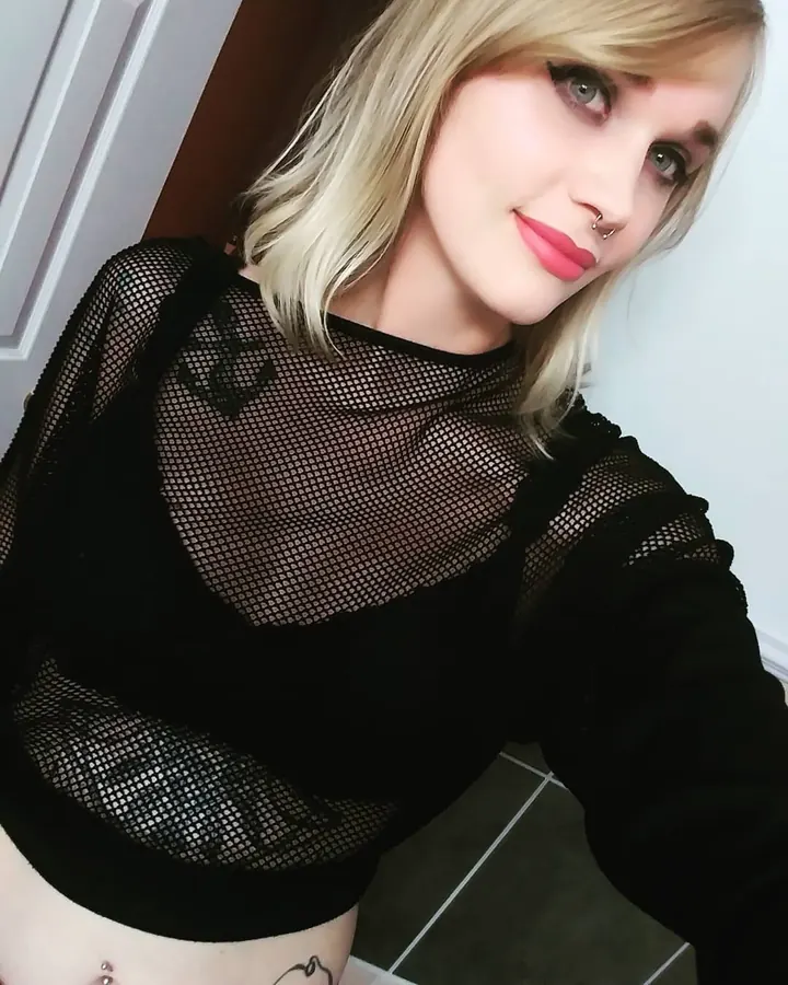 Jeune femme blonde en haut noir transparent, regardant l'appareil photo avec un sourire discret
