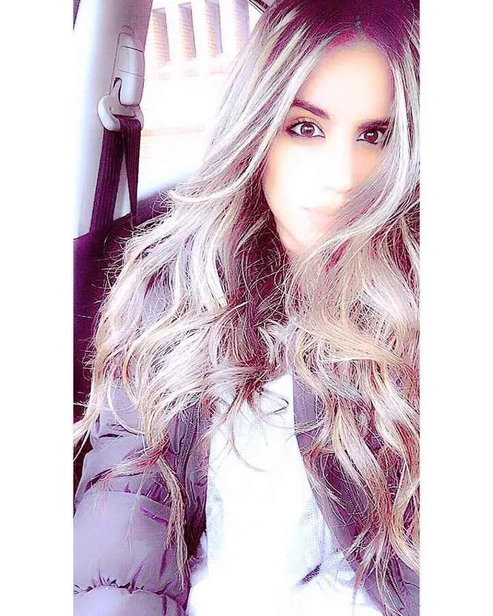 Femme aux cheveux gris, en veste grise, souriant, devant une fenêtre.