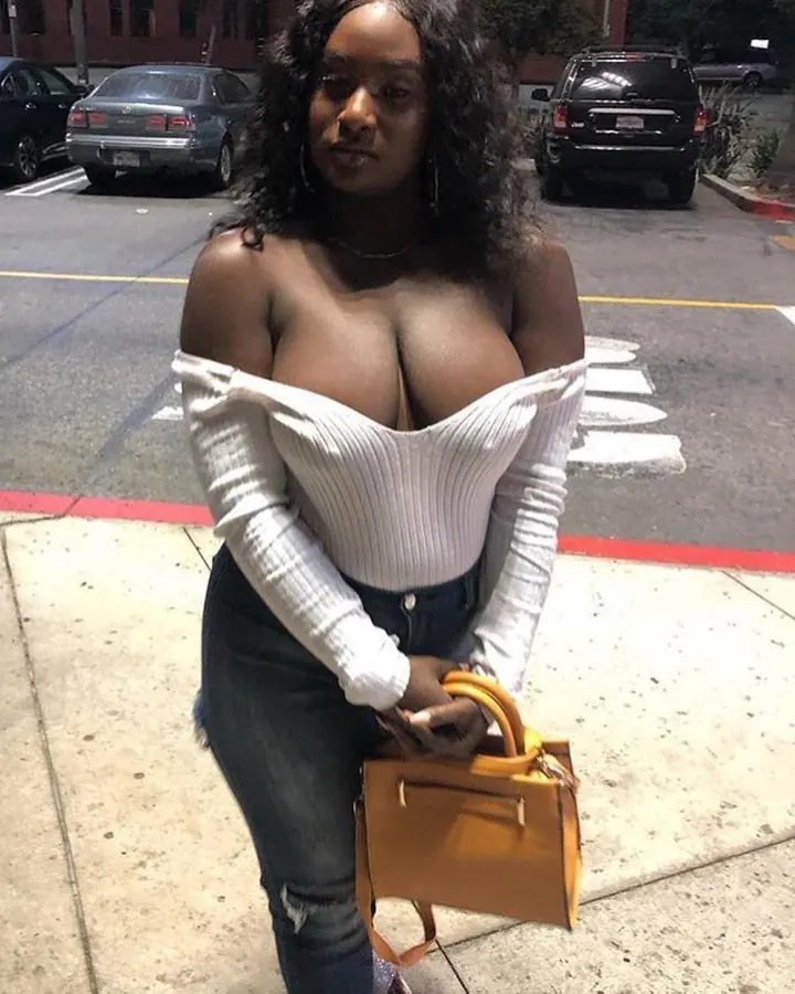 Femme aux cheveux noirs, en top blanc moulant et jeans, posant sur un trottoir avec une pochette jaune.