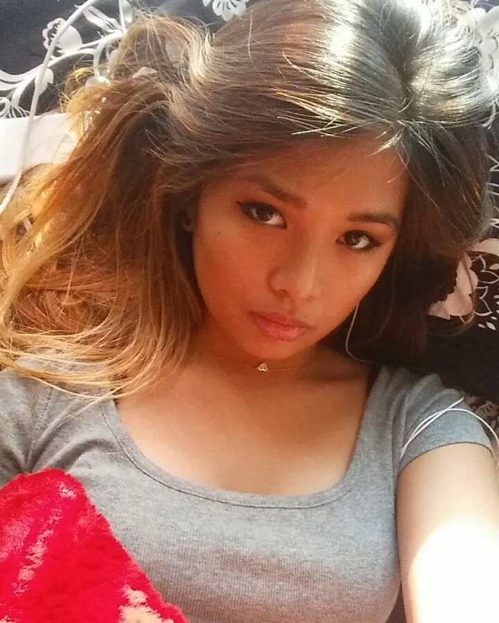 Femme asiatique en t-shirt gris, regardant l'appareil, cheveux ébouriffés, dans un lit.