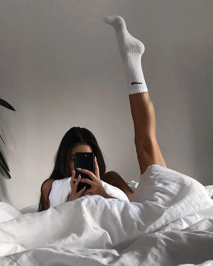 Femme brune en haut noir, prenant un selfie dans une chambre, regardant l'appareil.