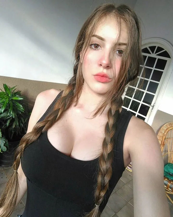 Jeune femme aux cheveux bruns en deux longues tresses, portant un haut noir, regardant directement l'appareil photo.