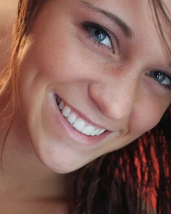 Jeune femme aux yeux bleus, souriante, regardant directement l’appareil photo, avec des cheveux bruns clairs.