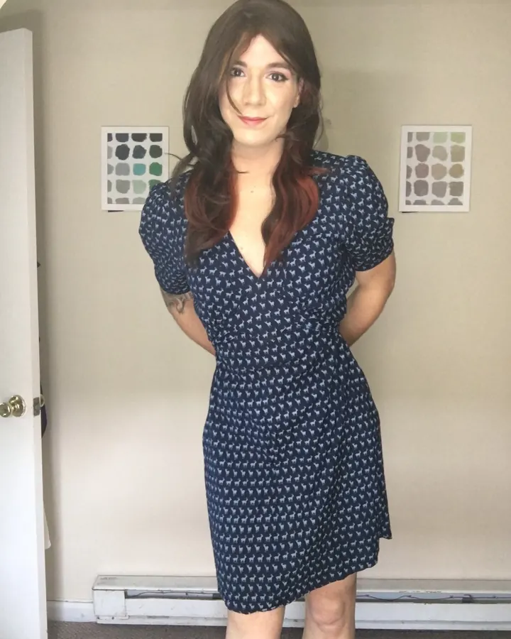Femme aux cheveux bruns, portant une robe bleue à motifs, posant dans une pièce lumineuse