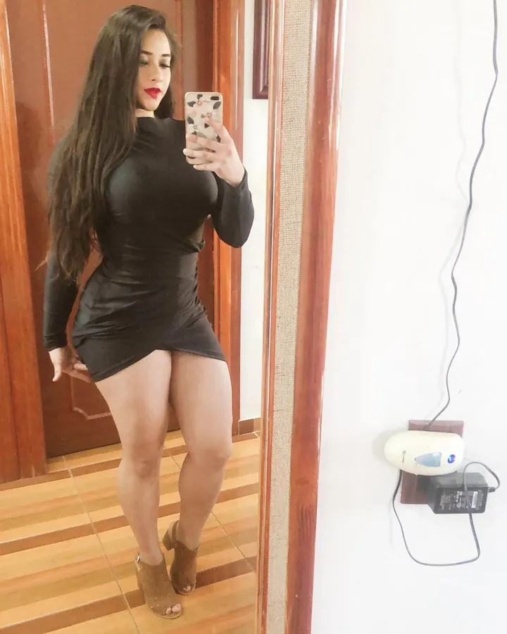 Femme aux cheveux bruns portant un haut noir à lacets, prenant un selfie dans un miroir.