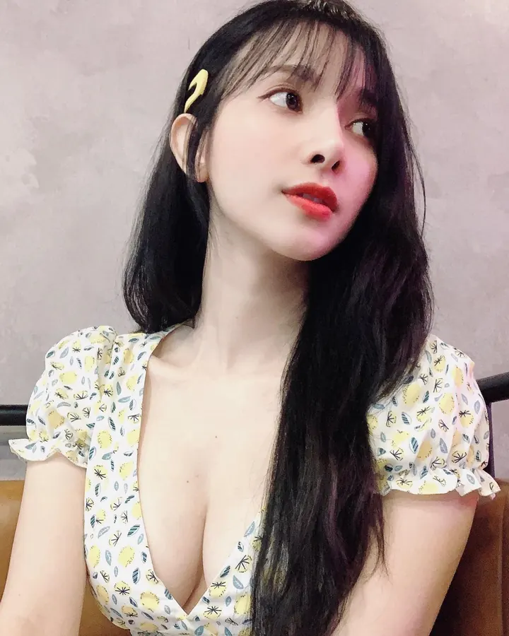 Femme asiatique, debout dans une pièce, portant un haut blanc et un short blanc en dentelle, tenant un téléphone noir, souriant légèrement.