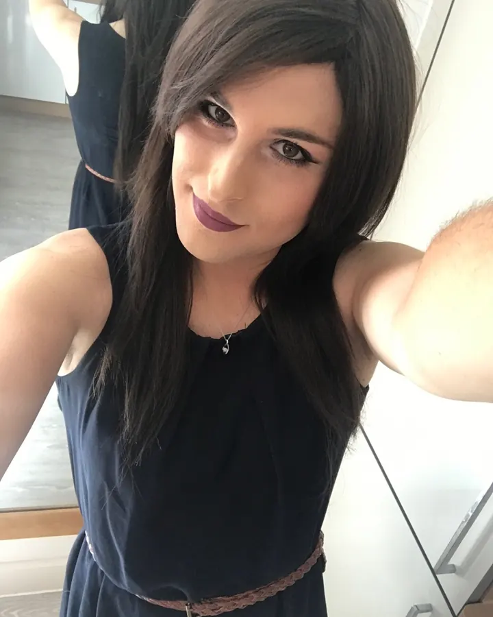 Femme aux cheveux bruns en haut rose, posant en intérieur.