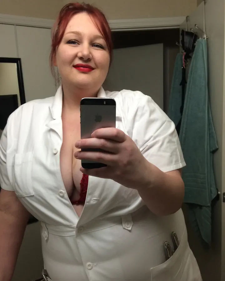Femme aux cheveux roux en haut noir, posant en extérieur.