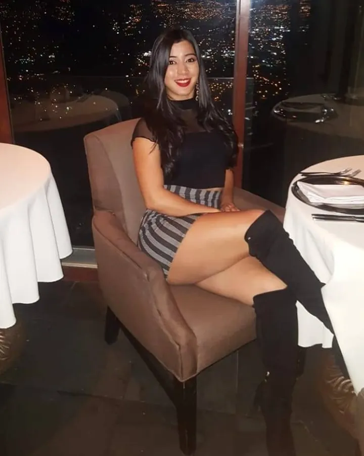 Femme aux cheveux noirs portant un haut noir et un short en jean, debout dos à la caméra sur une route.