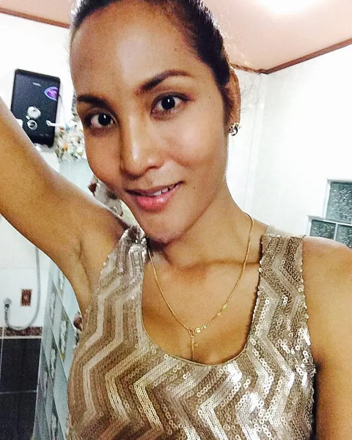 Femme en haut doré pailleté, souriante, prenant un selfie dans une pièce lumineuse.