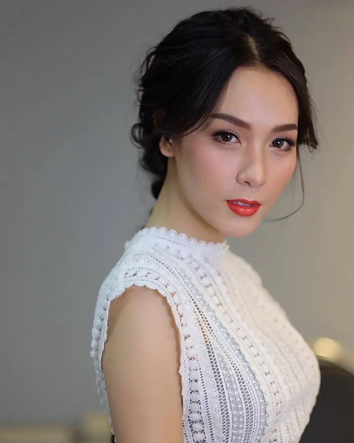 Femme asiatique aux cheveux noirs, vêtue d'une blouse en dentelle blanche, regardant l'appareil avec un léger sourire.