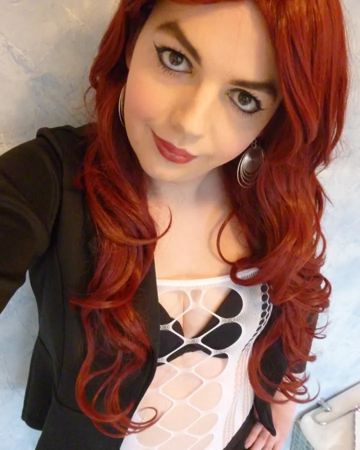 Femme aux cheveux roux prenant un selfie, portant une tenue noire et rouge avec une perruque rouge, regardant l'appareil photo.