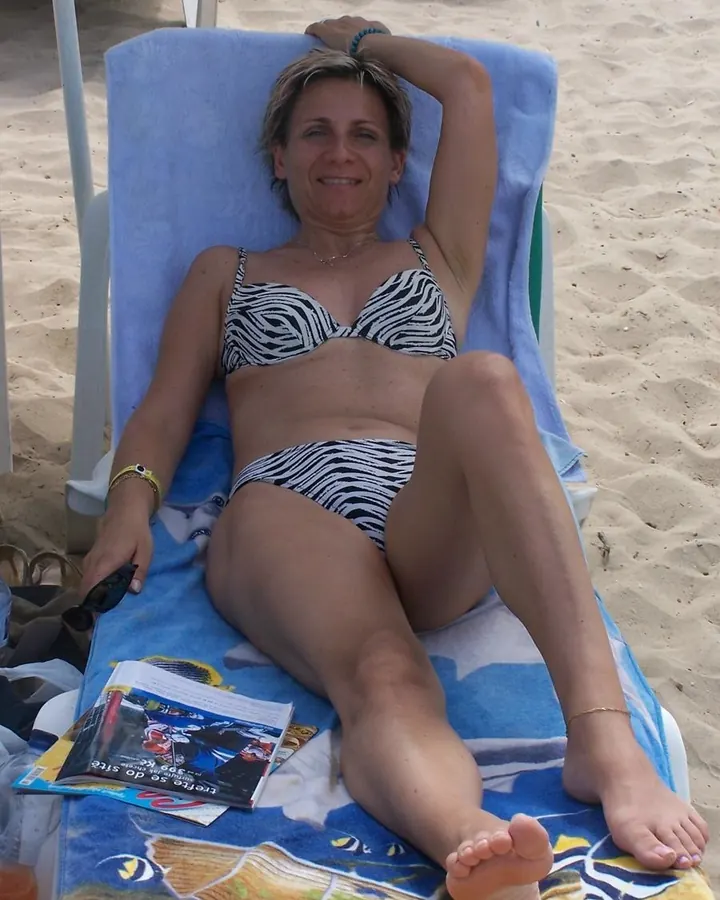 Femme aux cheveux blonds allongée sur une chaise longue au bord de la plage, portant un maillot de bain zébré.