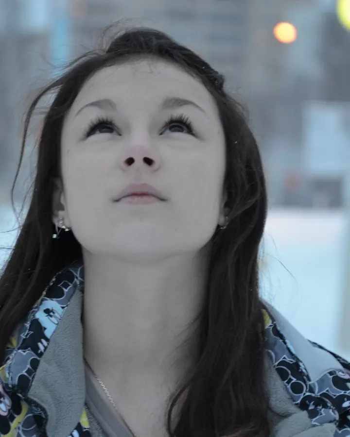 Jeune femme aux cheveux foncés, regard levé, debout dans la neige sous un éclairage urbain.