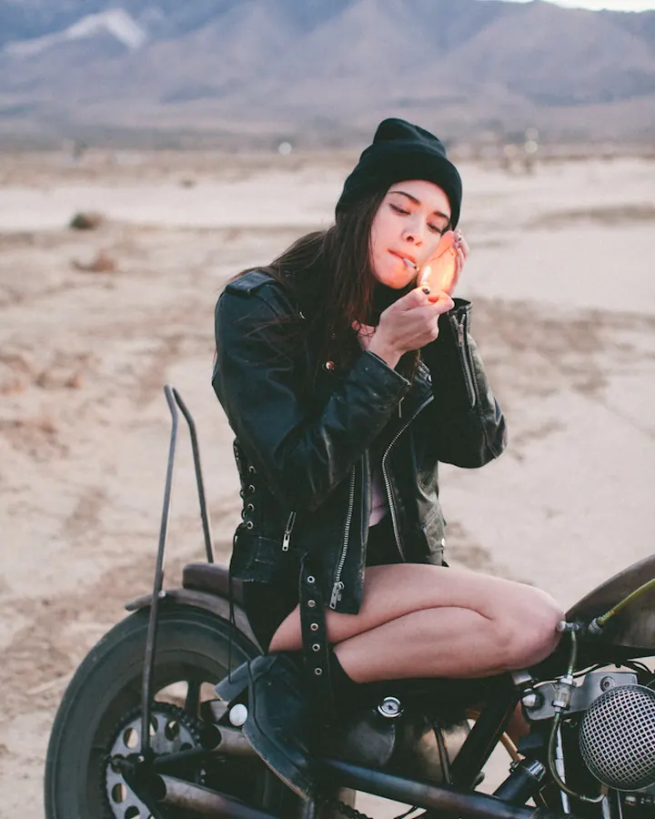 Femme en tenue de motarde, assise sur une moto dans un désert.