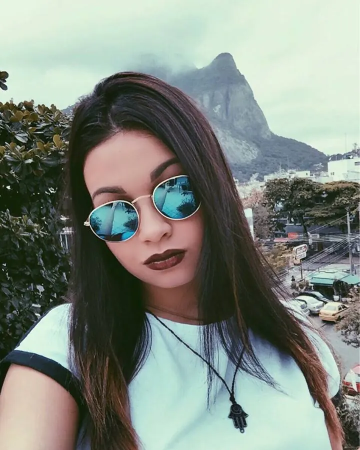 Femme aux yeux marrons et cheveux bruns-noirs, en haut violet, posant devant un dressing.