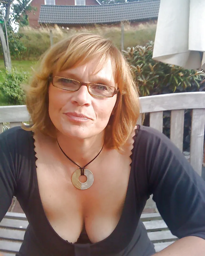 Femme en robe rouge ajustée, agenouillée sur un balcon en bois, souriant à l'appareil photo