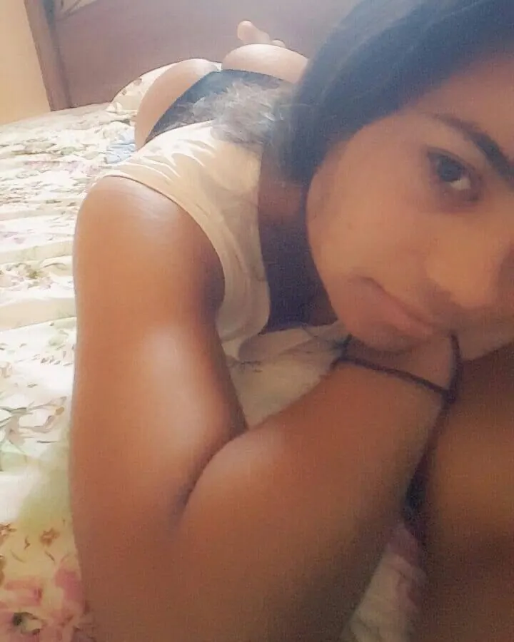 Jeune femme aux cheveux foncés allongée sur un lit, regardant l'appareil photo, vêtue d'un haut blanc