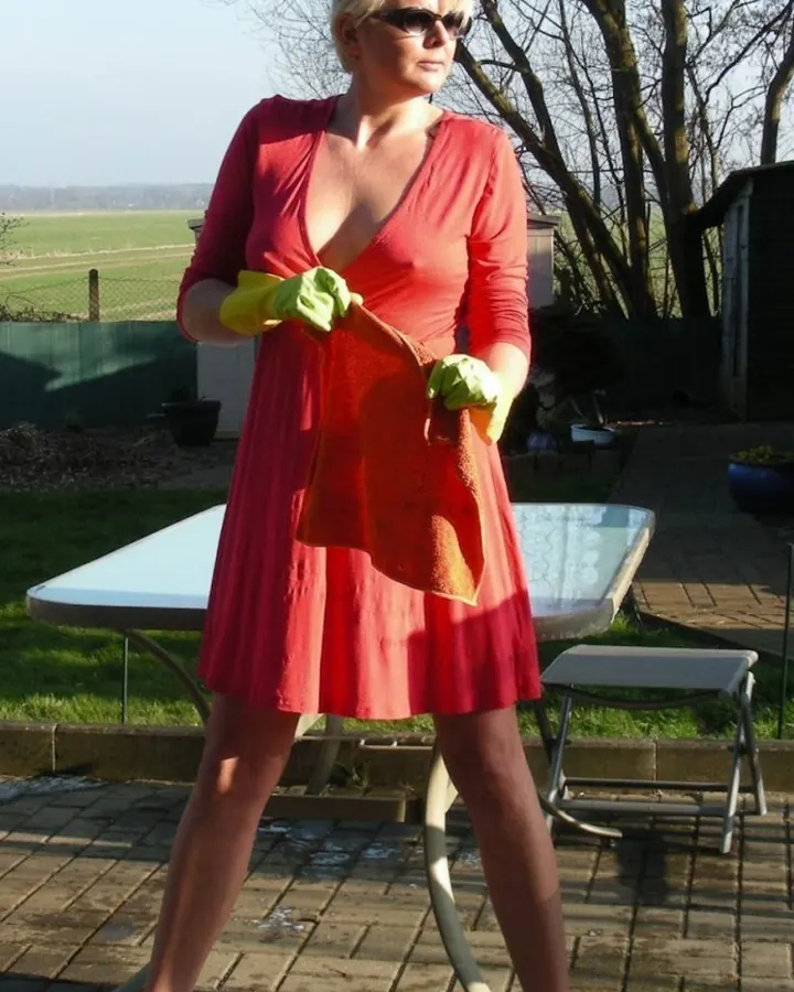 Femme aux cheveux blancs, en tenue de latex beige et noir, posant dans un intérieur, bras levés.