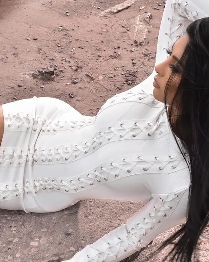 Femme aux cheveux bruns-noirs, portant un body blanc à lacets, allongée sur un sol terreux, regardant vers le ciel