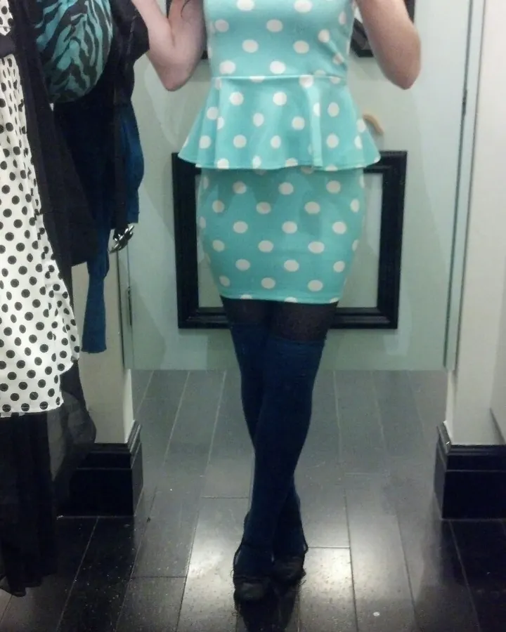Femme prenant un selfie devant un miroir, portant une robe bleu clair à pois blancs et des collants noirs.